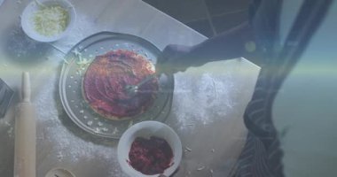 Domates sosu kepçeleyen ve tavada pizza kabuğuna konsantre halkalar serpiştiren bir adam. Pişirme, aşçılık, yemek hazırlama, gurme, rustik, el yapımı, malzeme