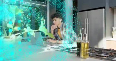 Adam mutfakta dizüstü bilgisayarda teknik işler yapıyor, olay yerinde turkuaz noktalar yazıp çalıştırıyor. Odaklanma, üretkenlik, kulaklıklar, kağıtlar, ada, modern ev