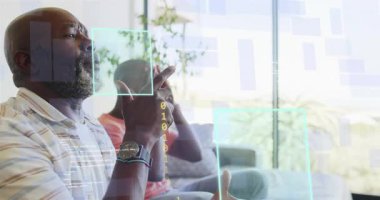 Baba ve oğul ekran teknisyeni tanıtımına, holografik UI izleme hareketlerine kanepede tepki veriyorlar. Aile, ev, güneş ışığı, modern, iç mekan, diyalog, bağ