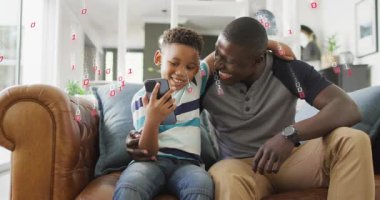 Baba ve oğul kanepede oturmuş telefonları dinliyorlar. Teknoloji ve öğrenmeyi gösteren ikili grafiklere sebep oluyorlar. Baba, çocuk, cihaz, eğitim, teknoloji, etkileşim, ev