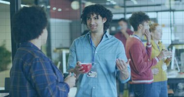 Açık mavi tişört giyen ve elinde monitörlü kırmızı bardak tutan kıvırcık saçlı adam. Ofis, iş arkadaşları, işbirliği, günlük, kahve, ekran, bardak