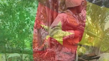 Cam zoom yapan asker, tüfeği ağaçların arasında göğsüne çeviriyor. Bayrak aynı hizadaki yıldız savunmayı gösteriyor. Savaşçı, kamuflaj, orman, bayrak, üç renkli, miğfer, güneş gözlüğü