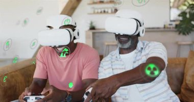 Baba ve yetişkin oğul, evde sanal gerçeklik oyunu oynarken yeşil hologramlar ortaya çıkıyor. Sanal, artırılmış, holografik, oyun, oturma odası, kanepe, arkadaşlar