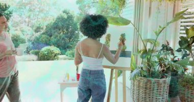 Ressam sehpada dikey darbeler uygulamaya başlıyor. Gözlemci kupayla giriyor, bitki sanatı yapıyor. Bahçe, bahçe, güneş ışığı, fırça işi, işbirliği, arkadaşlık, doğa