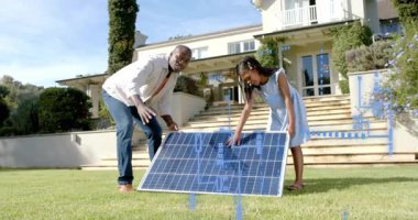 Erkek ve kız çimenlikteki güneş panelini kaldırıyor, mavi kaplamaları kullanarak enerjiyi öğretirken açıyı ayarlıyorlar. Açık hava, aile, yenilenebilir, gösteri, şematik, minimalist, banliyö