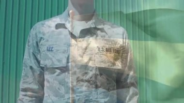 Erkek havacı ayakta duruyor, başını eğiyor sonra selamlıyor, bayrağı güneş amblemi ile selamlıyor ve sürükleniyor. Kamuflaj, ordu, üniforma, açık hava, pankart, sembol, parlak