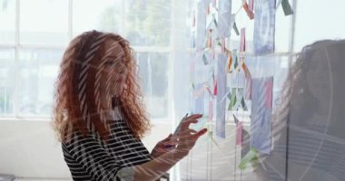 Dizayn stüdyosundaki cam duvarı sıralayan, mavi bloknotu kaldıran, sonra da canlandırılmış ışıltıyla notlar yapıştıran bir kadın. Arkaplan, yansıtıcı, düzenleyici, çalışma alanı, renkli, odaklı, fikir