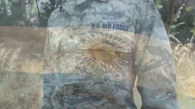 Havacı arka arkaya kameraya dönüyor, sağ elini kaldırıyor ve şeffaf güneş örtüsüyle selam veriyor. Ordu, kamuflaj, üniforma, açık hava, doğa, bayrak, amblem.