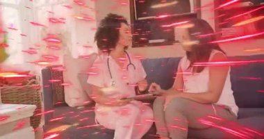 Hemşire tableti tutarken müşteri ekranı tıkırdatıyor. Bakım planını kırmızı kaplamayla gözden geçiriyor. Danışma, işbirliği, ev, oturma odası, steteskop, kanepe, empati