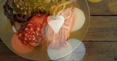 Bokeh ışıklarını kaydırmak çam kozalakları ve kalp etiketli yuvarlak tabakları ortaya çıkarıyor, kırsal dekoru gösteriyor. Topraksı, sıcak, ortam, düz döşeme, genel giderler, ahşap taneleri, süslemeler.