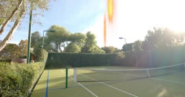 Güneşin büyümesi ve dikey turuncu parlamaların tenis kortunu ve ağını süpürüp aşırı açığa çıkarmasına neden oluyor. Açık hava, özel, çit, ağaçlar, çit, sokak lambası, lens.