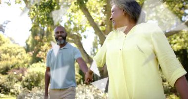 Parkta el ele tutuşan çift, reklamlar için göz teması kuruyor. Romantizm, olgunluk, açık hava, güneş ışığı, samimiyet, sıcaklık, doğa.