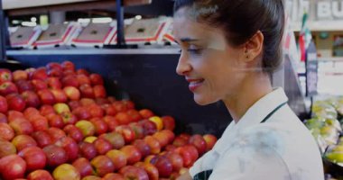Kadın ürün katibi yanlış sıralanmış elmaları fark ediyor ve kaliteyi kontrol ederken tekrar meyve sipariş ediyor. Süpermarket, düzenleme, denetleme, çalışan, raflar, tabela, parlak