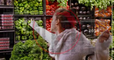 Erişen, yeşil biberi seçen, kırmızı HUD yıllarını kaplarken ürünü kontrol eden dişi alışverişçi. Sebzeler, süpermarket, müşteri, ekran, teftiş, hareketli, grafikler