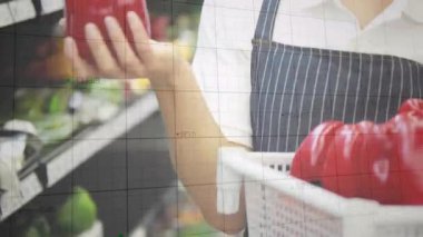 Kadın bakkal kırmızı biber seçiyor, yeşil grafikler rafı kaplarken tazeliği kontrol ediyor. Üretim, sebze, alışveriş, önlük, sepet, vitrin, pazar