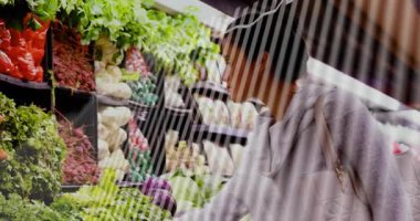 Yapraklı yeşillikleri fark eden bir kadın markete ulaşıyor ve inceliyor. Çerçeveyi çapraz çizgiler kaplıyor. Alışveriş, süpermarket, sebze, biber, karnabahar, patlıcan