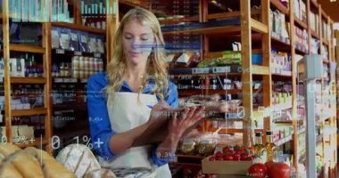 Kadın tezgahtar pano okuyor ve perakende satışta çizelgeler olarak yazıyor. Görünüyor ve stokları yönlendiriyor. Market, üretim, fırın, raflar, kırsal, sıcak, envanter