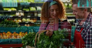 Sepet tutan kadın yeşilliklere uzanıyor mali tabloların yükselmesine neden oluyor. İkisi de gülümsüyor. Market, dükkan, önlükler, iş arkadaşları, takım çalışması, taze, portakal