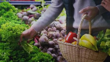 Alışverişci kadın yetişiyor, sebzeleri seçiyor, eşi sepeti tutuyor, koluna dokunuyor, alışveriş yapıyor. Çift, bakkal, süpermarket, koridor, muz, domates, biber