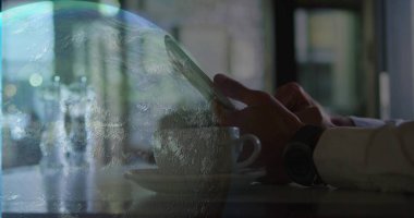 Kafede uzun kollu tişört giyen bir adamın ellerine dokunmak telefon, beyaz bardak, saat, gezegen örtüsü. Dokunmatik ekran, dünya, çift pozlama, iş, çay fincanı, saat, karamsar