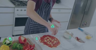 Pembe kaseden pizza yapan erkek ergen erkek, UI simgeleri tarife dikkat çekerken biber serpiyor. Yemek, mutfak, tezgah, önlük, solo, yakın çekim, hazırlık.