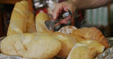 Baker çizgili önlük giyer ve müşteri talebi başına metal maşayla kruvasan toplar. Fırın, sıcaklık, köy, sepet, ekmek, yakın plan, iç mekan.