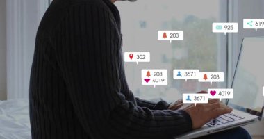 Pencerenin yanında dizüstü bilgisayarda yazan olgun bir adam, nişan dalgalanmasını gösteren yüzen sosyal rozetler üretiyor. Uzaktan, bildirimler, uyarılar, ekran, konsantrasyon, ana ofis, gün ışığı