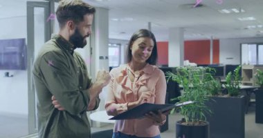 Siyah klasörü eğen ve ofiste sayfaları gösteren bir kadın, iş arkadaşı için proje detaylarını aydınlatıyor. İş arkadaşı, işbirliği, belge, çalışma alanı, monitörler, santraller, bölünme