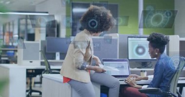 Dizüstü bilgisayarına çizelge çizen, iş verilerini HUD ile yazıp analiz eden bir kadın. İşbirliği, takım çalışması, ofis, açılış planı, çalışma istasyonu, monitörler, belgeler