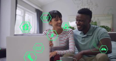 Kanepede oturan çift, enerji bilgilerini gösteren dizüstü bilgisayar izliyor, yeşil büyü simgeleri öğrenmeyi yönlendiriyor. Sürdürülebilirlik, ev, gün ışığı, ortaklık, eğitim, teknoloji, kaplama