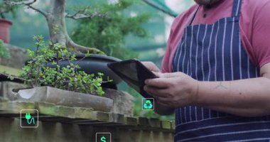 Bahçıvan bahçedeki tableti tıkırdatıyor, enerji ölçümlerini izliyor, bonsai 'de yüzen ikonlar. Arka bahçe, yeşillik, bahçıvanlık, ekoteknoloji, yenilenebilir, akıllı, mobil