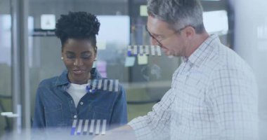 İşaret eden, kıvılcım saçan bir adam ofiste notlara camla bakıyor, grafiklerle rehberlik ediyor. İşbirliği, akıl hocalığı, takım çalışması, tartışma, planlama, bölünme, posta