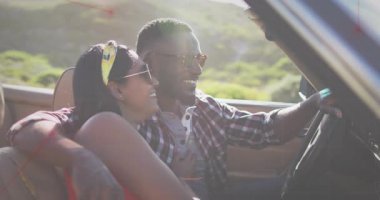 Erkek sürücü, kadın üstü açık arabaya yaslanıyor, güneş ışığı hareket güzergahını işaret eden hareketli fişeklere neden oluyor. Üstü açık araba, çift, yamaç, açık hava, güneşli, arka ışıklandırma, lens.