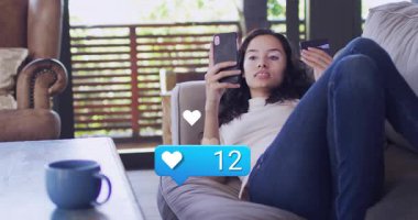 Kanepeye yaslanmış bir kadın telefonla mavi sosyal bildirimleri izliyor. Kalp atışları yükseliyor. Akıllı telefon, kart, oturma odası, ev, rahat, minimalist, doğal ışık