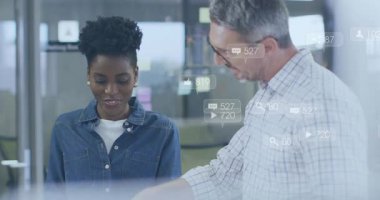 Kadın içeriği gözden geçirirken, erkek KPI 'leri açıklarken sosyal medya simgeleri yüzüyor. İşbirliği, ölçüler, akıl hocalığı, iş arkadaşları, ofis, cam, bölünme