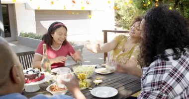 Veranda masasında oturan dört yetişkin, kadın parti sırasında cama uzanıp konfeti yakıyor. Grup, yaşam tarzı, samimi, açık hava, arka bahçe, kutlama, tost