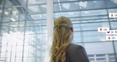 Duraklayan ve cam atriyuma bakan bir kadın. Kafasının etrafında büyüyen ikonlar sosyal medyada vızıltı gösteriyor. Şirket, lobi, yetki, liderlik, güven, ağ oluşturma, modern