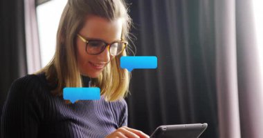 Tableti tıkırdatan, sohbet baloncukları çıkaran, teknolojide sohbet okuyan, gülümseyen ve bardakları ayarlayan bir kadın. Profesyonel, aygıt, pencere, doğal, çalışma alanı, odak, gözlük