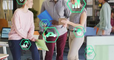 Ofisteki üç iş arkadaşı tablet tıklayarak ekolojik ölçümler için ekibin etrafında canlandırılmış veri simgelerini inceliyor. İşbirliği, açılış planı, modern, sürdürülebilirlik, görselleştirme, grafik, altıgen