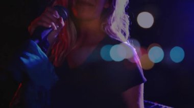 Kadın şarkıcı mikrofon büyütüyor ve şarkı söylüyor, loş sahnede müzik yapıyor, Bokeh ışıkları kesişiyor. Kapanış, vokalist, performans, spot ışığı, karamsar, samimi, mekan