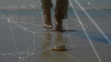 Alçak açılı çıplak ayaklar ıslak kumda yürüyor, kabuğu görüyor, yavaşlıyor ve kaldırmak için uzanıyor, hareket ediyor. Plaj, deniz manzarası, kıyı şeridi, çakıl taşı, taş, ayak sesleri, tefekkür