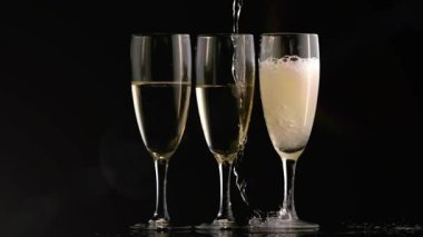 Yukarıdan akan akıntı 3 flütün üzerinde kayar kabarcıklar oluşturur, köpüklü kafaları yaratır, alevler hareket eder. Stemware, şampanya, ışıltı, yansımalar, minimalist, stüdyo, zarafet