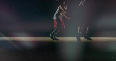 12 numaralı oyuncu topu top çalmaktan ve top çalmaktan koruyor. Defans oyuncusu yaklaşıyor, çemberin altına giriyor. Basketbol, sporcular, teke tek savunma, hücum, mahkeme, ışıklandırma.