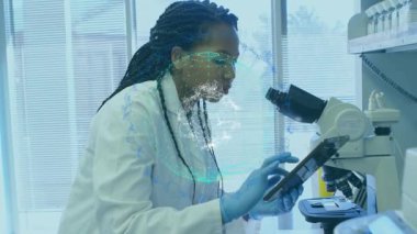 Kadın araştırmacı tableti tıklatıyor ve göz merceğine bakıyor. DNA kaplamalı örnekleri inceliyor. Mikroskop, laboratuvar, bilim adamı, eldivenler, labirent, dokunmatik ekran, genetik