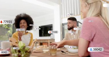 Masadaki grup, bir kadeh kaldırma, sosyal medya rozetleri insanların etrafında uçuşuyor, kadeh kaldırıyor. Arkadaşlar, yemek, ev, güneş ışığı, modern, parlak, bildirimler