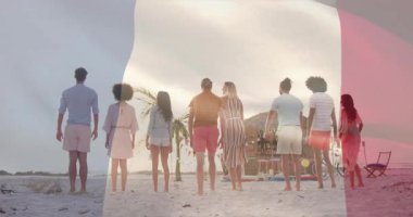 8 yetişkin kollarını birleştiriyor, seyahat için sahilde zıplıyor, grubun üzerinde üç renkli bayrak dalgalanıyor. Dostlar, sahil kenarı, gün batımı, kum, avuç içi, bayrak, sıçrayış