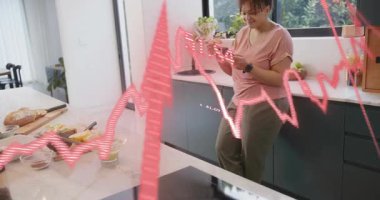 Mutfakta eğilip telefonu dinleyen ve diyet takibi için kırmızı grafiği etkinleştiren bir kadın. Ev, modern, yaşam tarzı, refah, aygıt, gündelik, beslenme