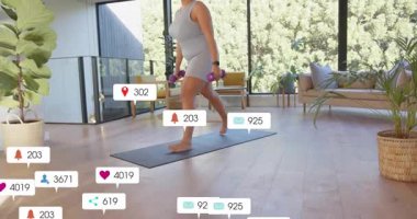 Spor salonundaki kadın gri paspasa basıyor mor ağırlıklarla hamleler yapıyor, görünmeyi seviyor, manzarayı yükseltiyor. Dambıllar, kardiyo, genel giderler, denge, modern, güneş ışığı, ev