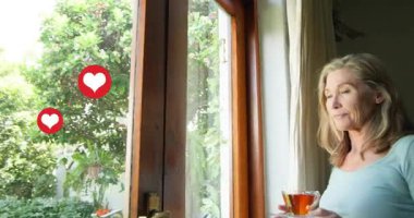 Kadın perdeyi çekiyor, yüzen kalplere sebep oluyor, bardağı tutuyor, pazarlama için kaldırıyor ve yudumluyor. Sakin, bahçe, pencere, çay, bardak, sakin, düşünceli