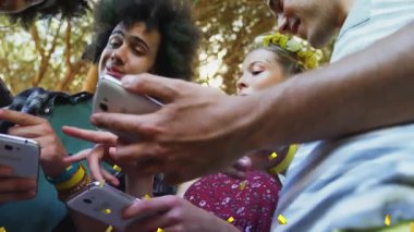 Ağaçların altında telefonları dinleyen ve sosyal paylaşımda bulunan beş arkadaş sarı konfeti örtüsü oluşturuyor. Grup, açık hava, festival, samimi, aygıtlar, etkileşim, konfeti